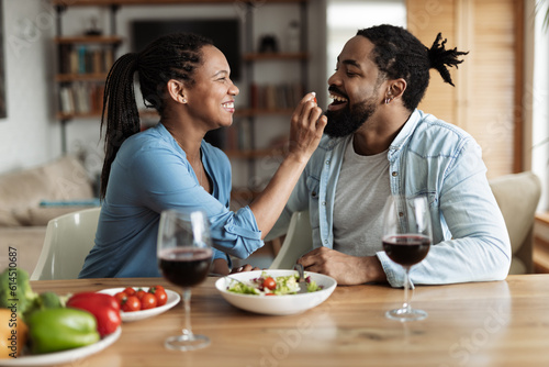Happy black woman feeding her boyfriend with salad during lunch in dining room