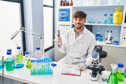 Young arab man scientist write on document analysing lentils test tube at laboratory