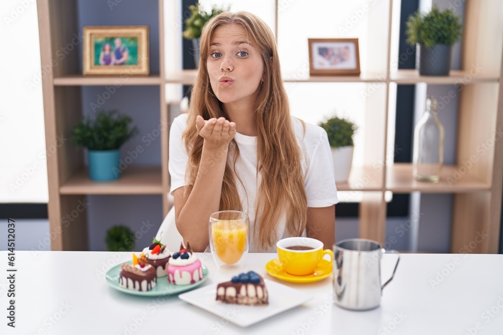 Young caucasian woman eating pastries t for breakfast looking at the camera blowing a kiss with hand on air being lovely and sexy. love expression.