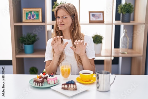 Young caucasian woman eating pastries t for breakfast disgusted expression, displeased and fearful doing disgust face because aversion reaction. with hands raised