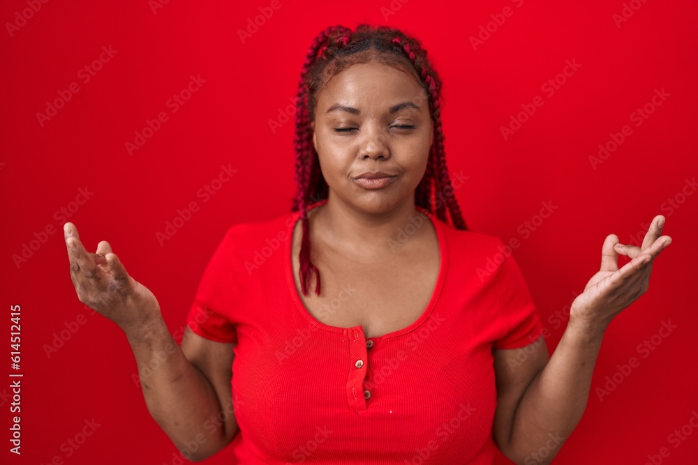 African american woman with braided hair standing over red background relax and smiling with eyes closed doing meditation gesture with fingers. yoga concept. African american woman with braided hair standing over red background relax and smiling with eyes closed doing meditation gesture with fingers. yoga concept.