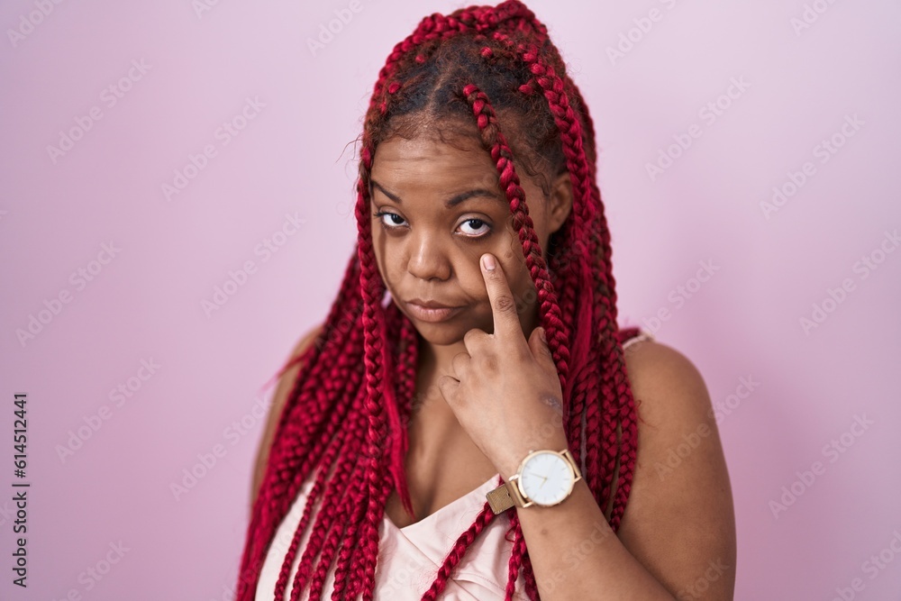 African american woman with braided hair standing over pink background pointing to the eye watching you gesture, suspicious expression African american woman with braided hair standing over pink background pointing to the eye watching you gesture, suspicious expression