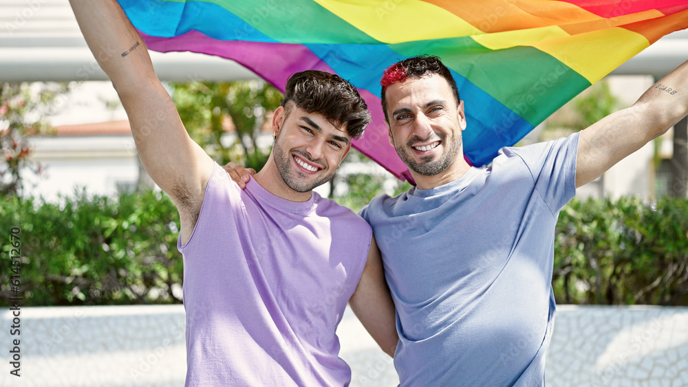 Two men couple hugging each other holding homosexual flag at park Two men couple hugging each other holding homosexual flag at park