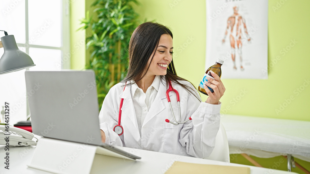 Young beautiful hispanic woman doctor using laptop holding medication bottle at clinic Young beautiful hispanic woman doctor using laptop holding medication bottle at clinic
