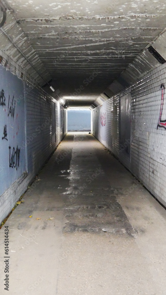 Tunnel souterrain et de traversée grande route sombre, peu lumineux, triste, lugubre, vide, pas rassurant, coin à piège, avec des murs a carreaux tagués, le bout du tunnel, sol mouillé et flaque d'eau