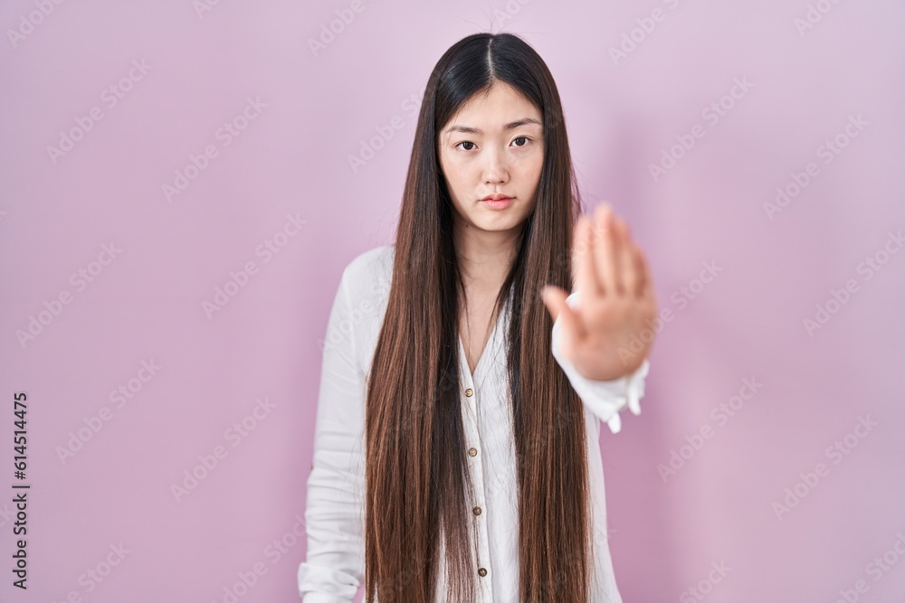 Chinese young woman standing over pink background doing stop sing with palm of the hand. warning expression with negative and serious gesture on the face. Chinese young woman standing over pink background doing stop sing with palm of the hand. warning expression with negative and serious gesture on the face.