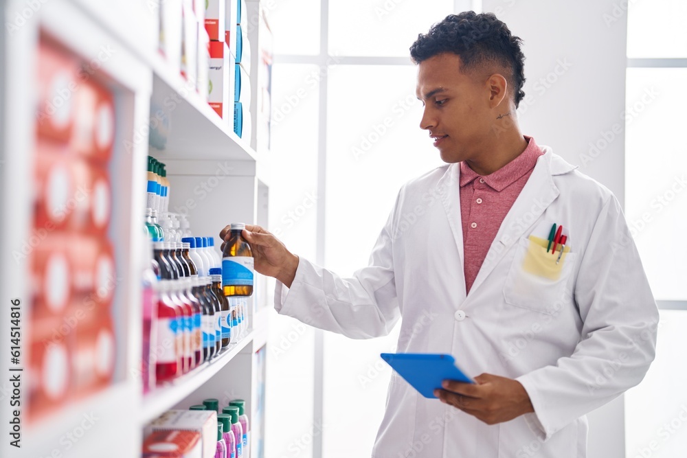 Young latin man pharmacist using touchpad holding medicine bottle at pharmacy