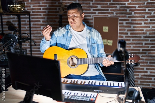 Hispanic young man playing classic guitar at music studio doing italian gesture with hand and fingers confident expression