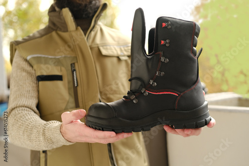 black work boots made of leather with reinforced cape, high top in hands of young bearded man, builder in uniform, concept of highest product quality, special shoes for different professions photo