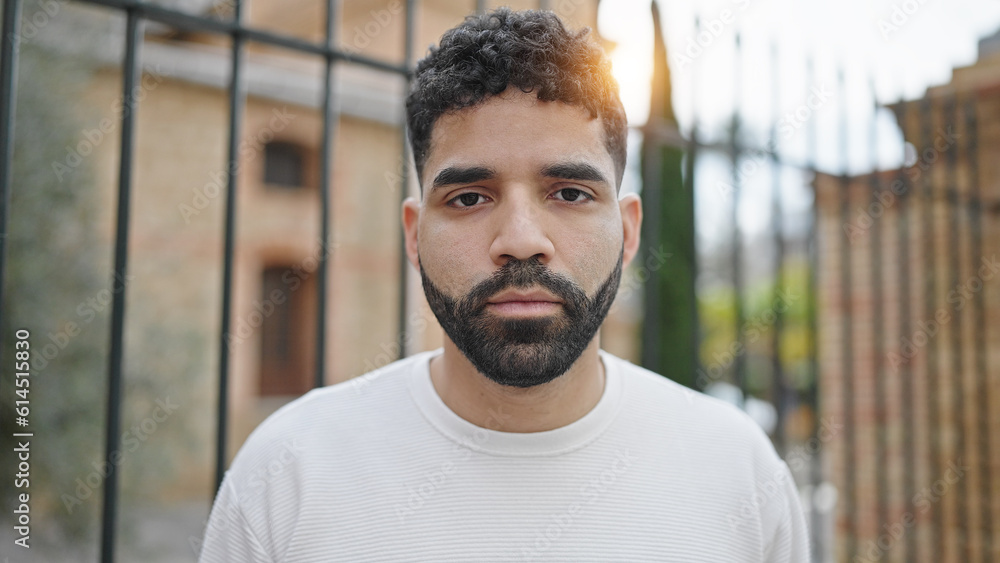 Young hispanic man standing with serious expression at street