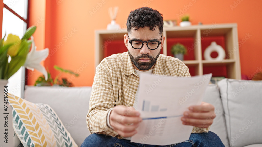 Obraz premium Young hispanic man reading document sitting on sofa at h