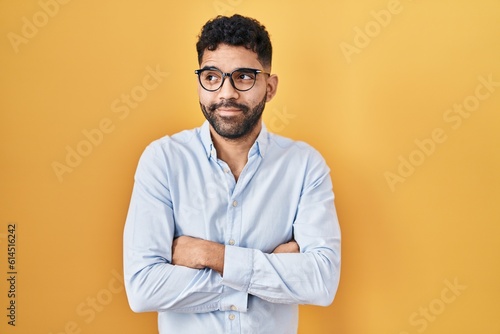 Hispanic man with beard standing over yellow background smiling looking to the side and staring away thinking.