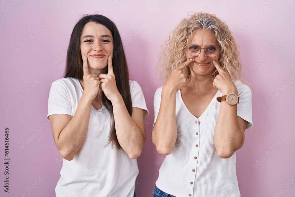 Mother and daughter standing together over pink background smiling with open mouth, fingers pointing and forcing cheerful smile Mother and daughter standing together over pink background smiling with open mouth, fingers pointing and forcing cheerful smile