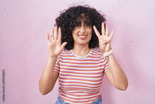 Young middle east woman standing over pink background showing and pointing up with fingers number nine while smiling confident and happy.