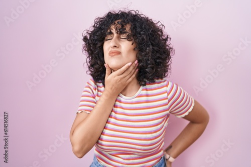 Young middle east woman standing over pink background touching painful neck, sore throat for flu, clod and infection