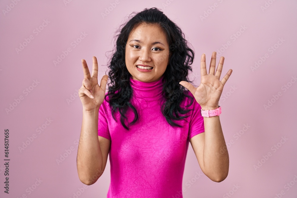 Young asian woman standing over pink background showing and pointing up with fingers number eight while smiling confident and happy. Young asian woman standing over pink background showing and pointing up with fingers number eight while smiling confident and happy.
