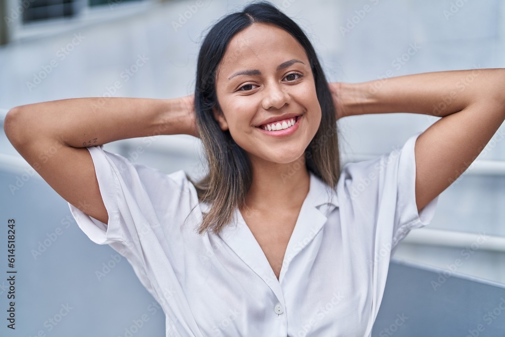 Young hispanic woman smiling confident relaxed with hands on head at street