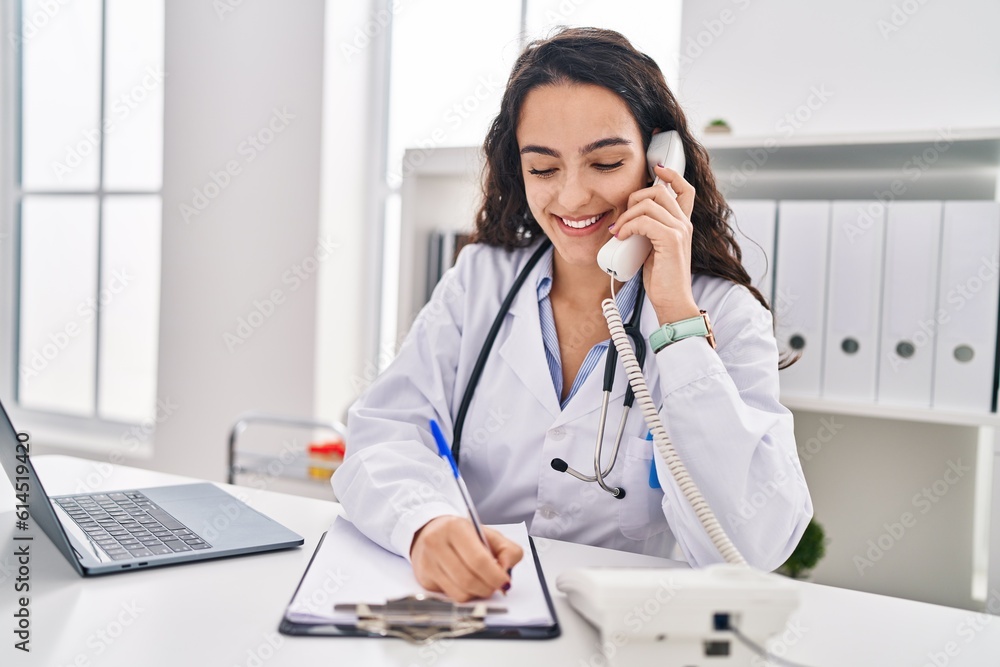 Young hispanic woman wearing doctor uniform talking on the telephone at clinic Young hispanic woman wearing doctor uniform talking on the telephone at clinic