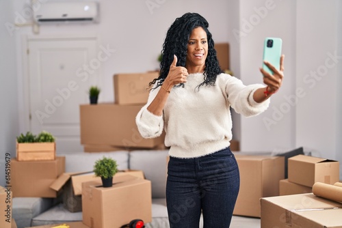 Middle age hispanic woman moving to a new home taking selfie picture smiling happy and positive, thumb up doing excellent and approval sign