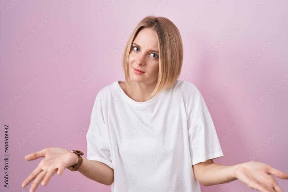 Obraz premium Young caucasian woman standing over pink background clueless and confused with open arms, no idea concept.