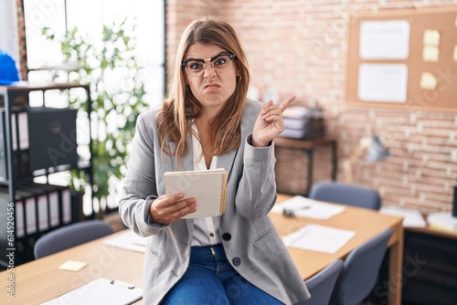 Young hispanic woman working at the office wearing glasses pointing aside worried and nervous with forefinger, concerned and surprised expression © Krakenimages.com