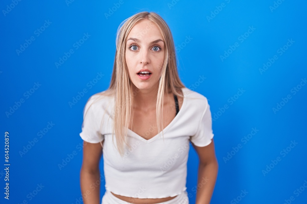 Young caucasian woman standing over blue background afraid and shocked with surprise and amazed expression, fear and excited face. Young caucasian woman standing over blue background afraid and shocked with surprise and amazed expression, fear and excited face.