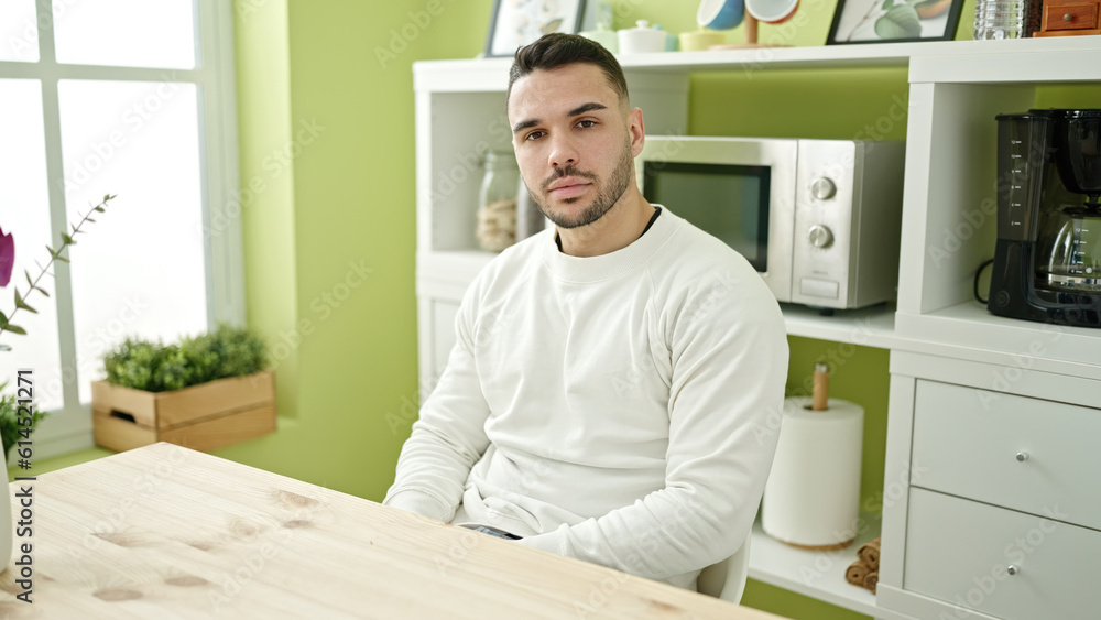 Young hispanic man sitting on table with serious expression at dinning room