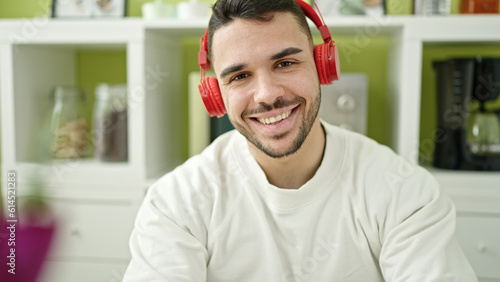 Young hispanic man listening to music sitting on table at dinning room