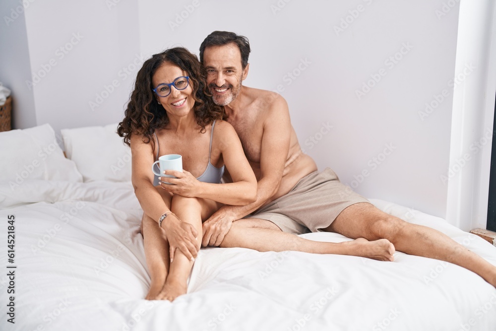 Man and woman couple drinking cup of coffee sitting on bed at bedroom Man and woman couple drinking cup of coffee sitting on bed at bedroom