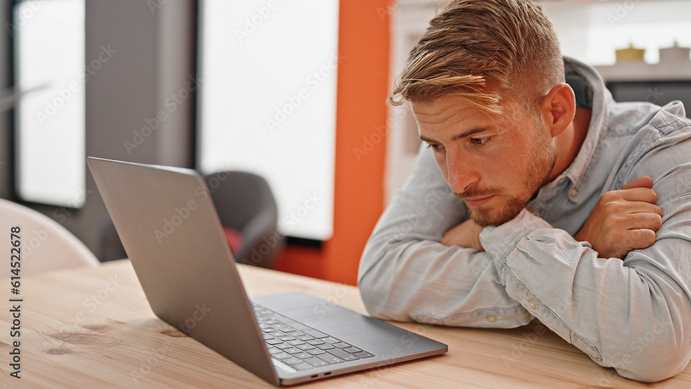 Young caucasian man using laptop sitting on table with sad express at dinning room Young caucasian man using laptop sitting on table with sad express at dinning room