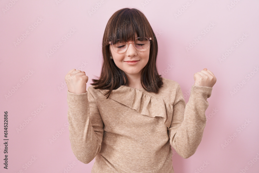 Little hispanic girl wearing glasses very happy and excited doing winner gesture with arms raised, smiling and screaming for success. celebration concept. Little hispanic girl wearing glasses very happy and excited doing winner gesture with arms raised, smiling and screaming for success. celebration concept.