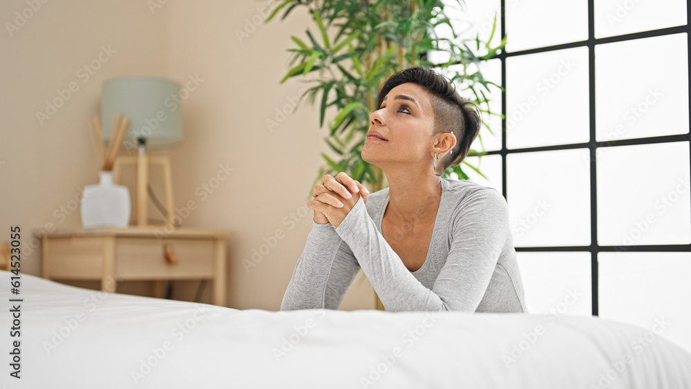 Young beautiful hispanic woman praying sitting on floor at bedroom