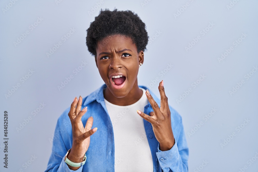 Φωτογραφία African american woman standing over blue background crazy and mad shouting and yelling with aggressive expression and arms raised
