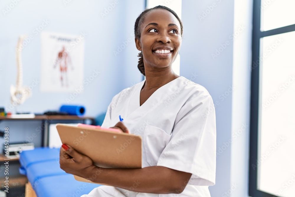African american woman physiotherapist smiling confident writing medical report at rehab clinic
