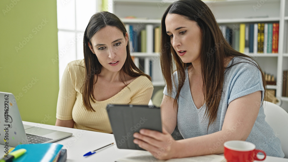 Two women sitting on table studying using laptop and touchpad at library university Two women sitting on table studying using laptop and touchpad at library university