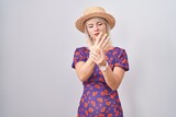 Young caucasian woman wearing flowers dress and summer hat suffering pain on hands and fingers, arthritis inflammation