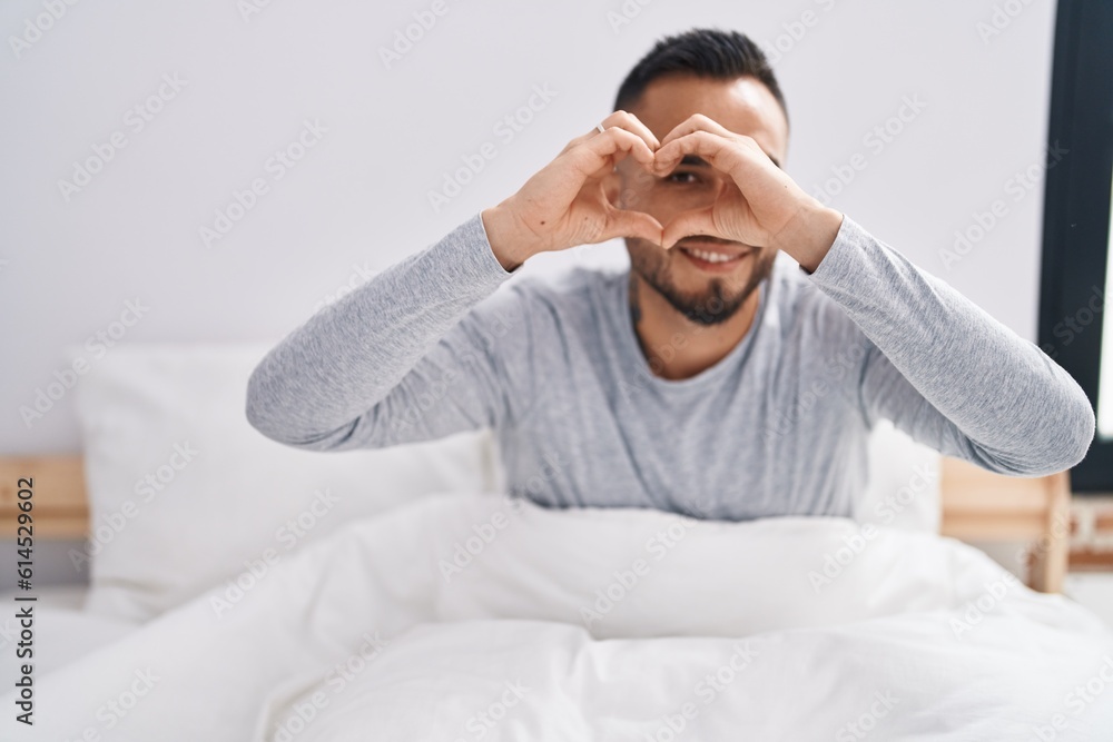 Young hispanic man doing heart gesture sitting on bed at bedroom Young hispanic man doing heart gesture sitting on bed at bedroom