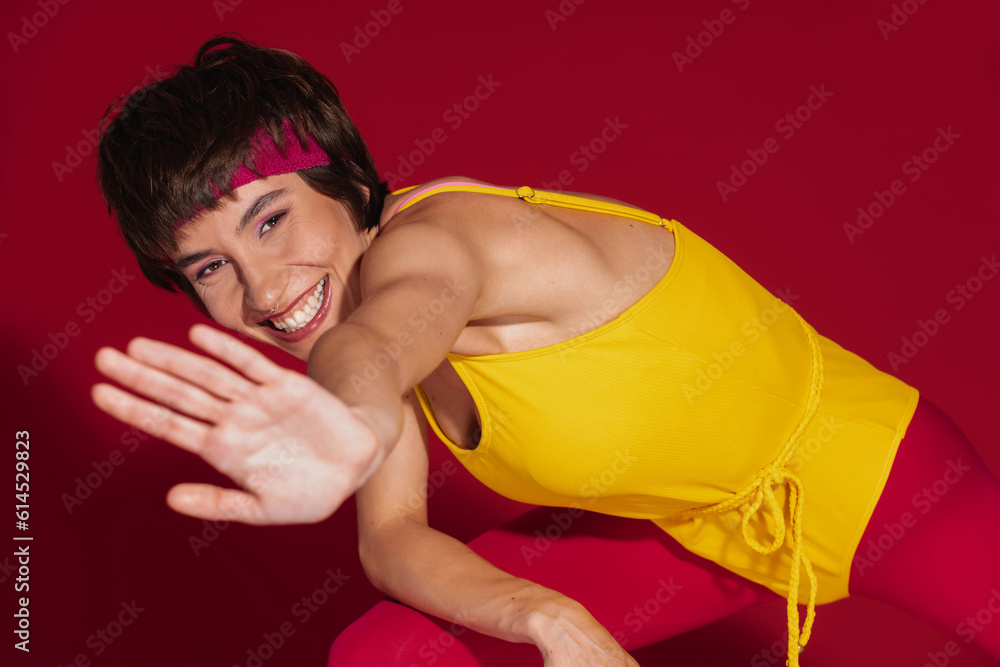 Happy young fit woman in retro styled sportswear stretching out hand against red background
