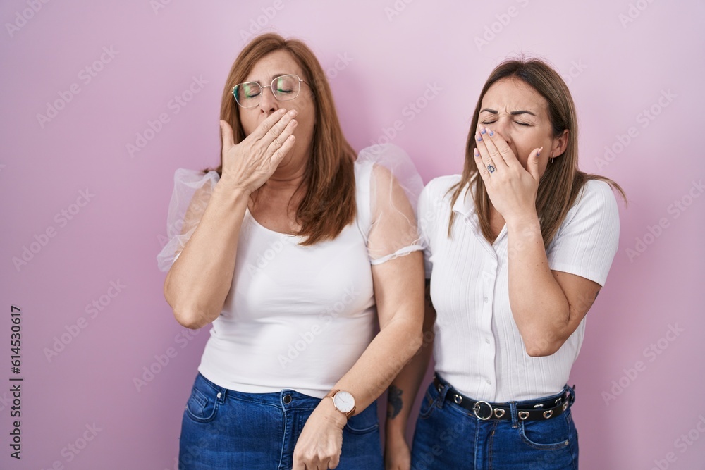 Hispanic mother and daughter wearing casual white t shirt over pink background bored yawning tired covering mouth with hand. restless and sleepiness. Hispanic mother and daughter wearing casual white t shirt over pink background bored yawning tired covering mouth with hand. restless and sleepiness.