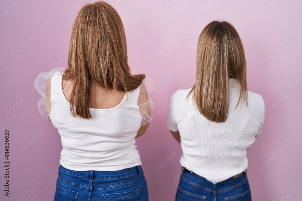 Hispanic mother and daughter wearing casual white t shirt over pink background standing backwards looking away with crossed arms Hispanic mother and daughter wearing casual white t shirt over pink background standing backwards looking away with crossed arms