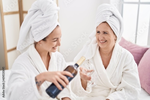 Mother and daughter wearing bathrobe drinking wine at bedroom