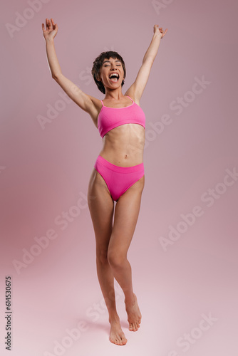 Full length of happy young short hair woman in underwear gesturing against colored background