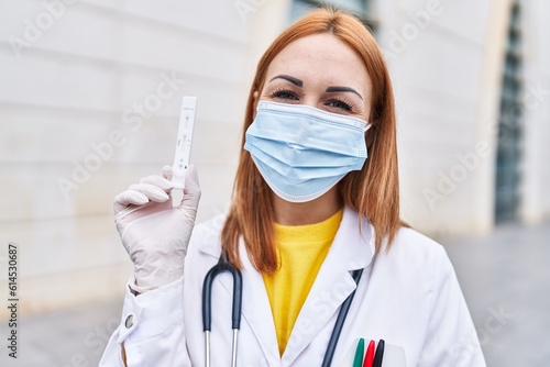 Young doctor woman holding coronavirus infection test looking positive and happy standing and smiling with a confident smile showing teeth