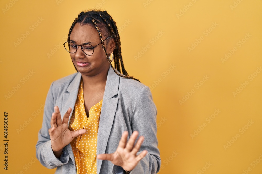 African american woman with braids standing over yellow background disgusted expression, displeased and fearful doing disgust face because aversion reaction. with hands raised African american woman with braids standing over yellow background disgusted expression, displeased and fearful doing disgust face because aversion reaction. with hands raised