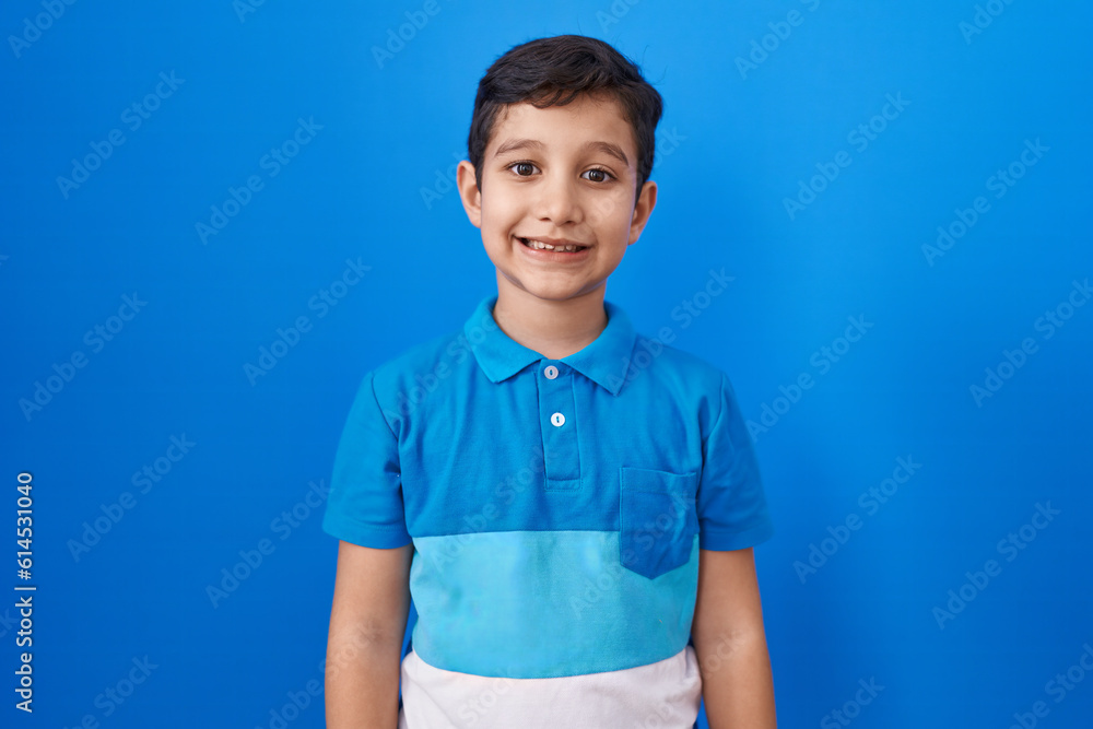 Little hispanic boy standing over blue background with a happy and cool smile on face. lucky person.