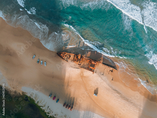 High angle aerial bird's eye drone view of the Maheno shipwreck on Seventy-Five Mile Beach on Fraser Island, Queensland, Australia. Beautiful sunset light with waves.
