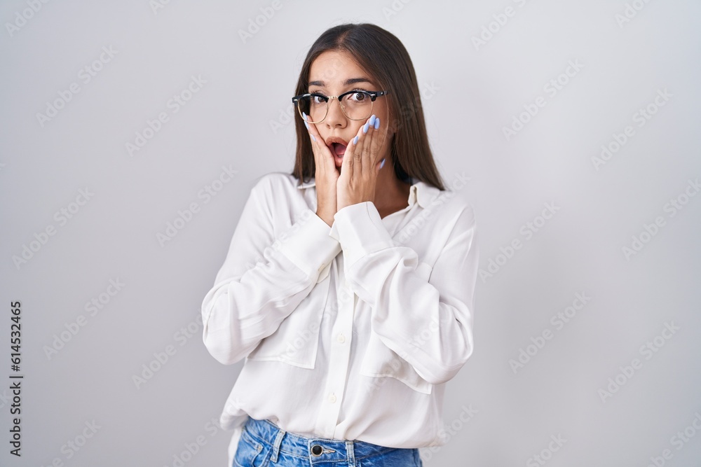 Young brunette woman wearing glasses afraid and shocked, surprise and amazed expression with hands on face Young brunette woman wearing glasses afraid and shocked, surprise and amazed expression with hands on face