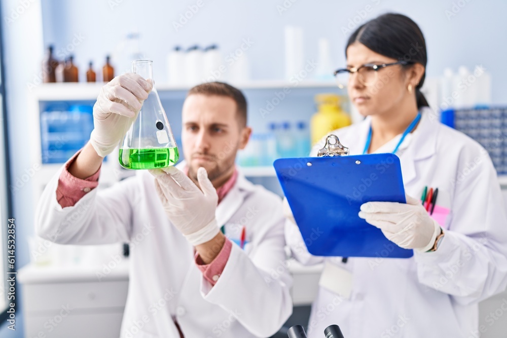 Man and woman wearing scientists uniform measuring liquid at laboratory Man and woman wearing scientists uniform measuring liquid at laboratory