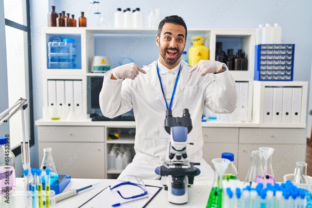 Young hispanic man with beard working at scientist laboratory looking confident with smile on face, pointing oneself with fingers proud and happy. Young hispanic man with beard working at scientist laboratory looking confident with smile on face, pointing oneself with fingers proud and happy.