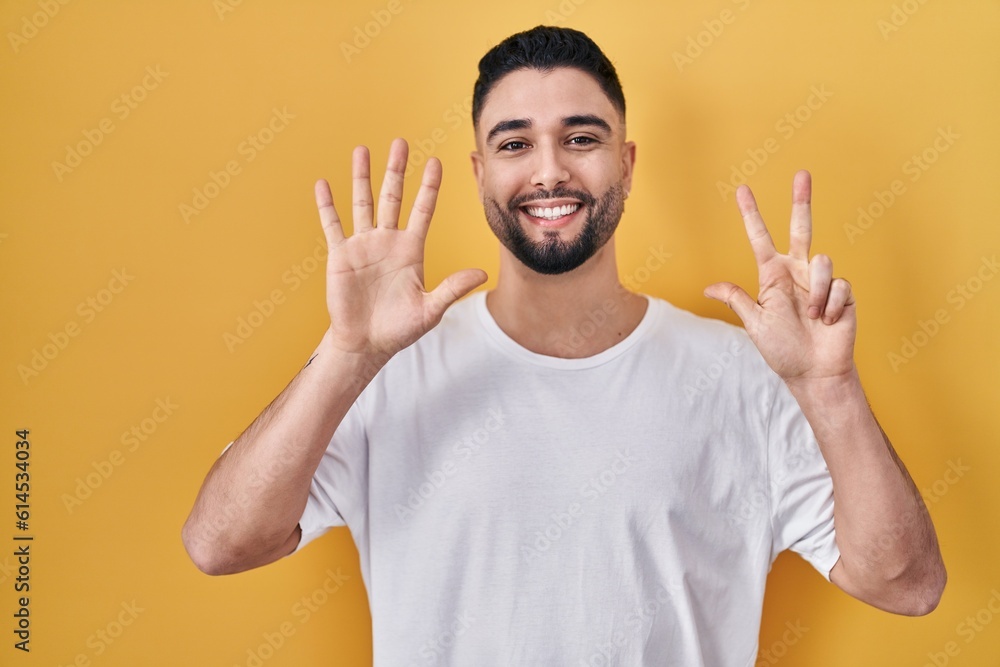 Young handsome man wearing casual t shirt over yellow background showing and pointing up with fingers number eight while smiling confident and happy. Young handsome man wearing casual t shirt over yellow background showing and pointing up with fingers number eight while smiling confident and happy.